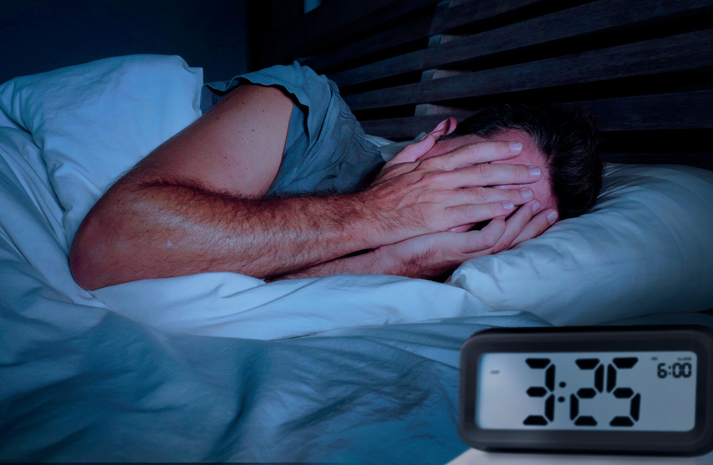 Mann wird mitten in der Nacht wach und hält sich die Hände vors Gesicht